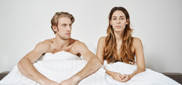 Paar im Bett mit frustriertem Gesichtsausdruck