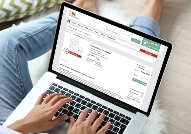Ein Laptop liegt auf einem Schoß, zwei Hände tippen auf der Tastatur. Auf dem Bildschirm der Online-Shop der ABF-Apotheke